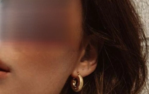 Close-up of golden snail-shell textured hoop earring on a model ear in warm light