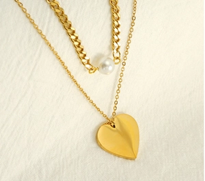 Close-up of double-layered gold necklace with heart pendant and white pearl detail