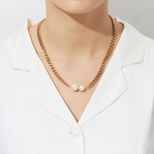 Close-up of golden chunky chain necklace with two white pearls on a model wearing white suit