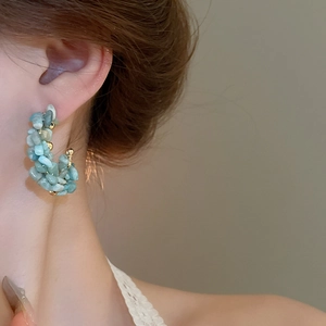 Close-up of model wearing C-shaped earrings with light blue stones and gold beads