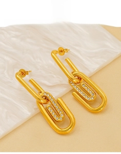 Détail des boucles d'oreilles trombone dorées avec strass brillants sur un plateau blanc