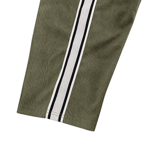 Close-up of olive green corduroy trousers featuring side black and white stripes
