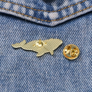 Golden whale-shaped alloy brooch with butterfly clasp pin on blue denim fabric background