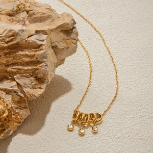 Detail of 18K gold stainless steel necklace with round white pendant and zircon on beige rock