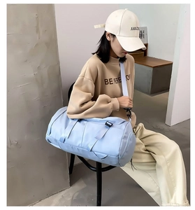 Detailed side view of a light blue cylindrical travel bag with adjustable strap and handle