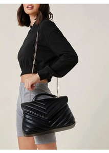 Close-up of black quilted leather shoulder bag with gold chain and V-pattern stitching