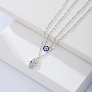 Detail of s925 silver double necklace featuring Evil Eye and Hamsa Hand charms with blue stones