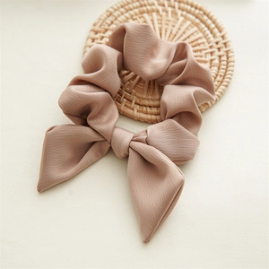 Close-up of pink bow scrunchie with pleated texture on rustic woven coaster