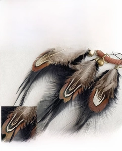 Detailed close-up of natural feathers and bronze bells on a handmade dreamcatcher car charm