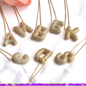 Flat lay of multiple micro-pave gold initial necklaces on pink silk background