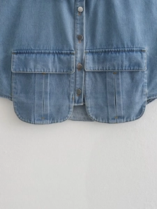 Vue détaillée des boutons en métal et grandes poches à rabat sur chemise denim sans manches