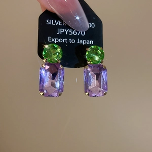 Macro detail of silver geometric earrings with round green and purple faceted stones