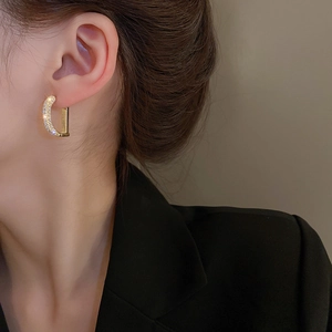 Detailed view of D-shaped gold earrings with pavé zircons worn on model's ear