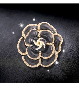 Détail macro d'une broche camélia noir avec perles blanches sur pétales dorés à l'or