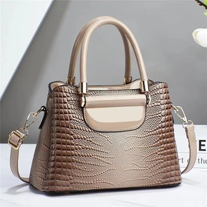 Detail of glossy beige crocodile embossed bucket bag with gold hardware and dual handles