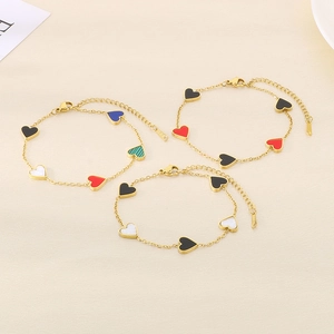 Three gold heart charm bracelets with colorful enamel insets on soft beige fabric