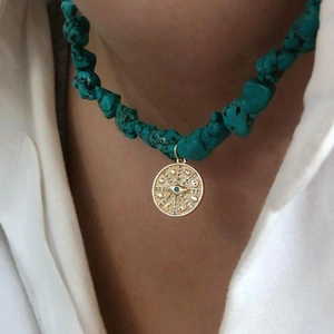 Macro shot of turquoise beaded necklace featuring a gold evil eye pendant on a white shirt