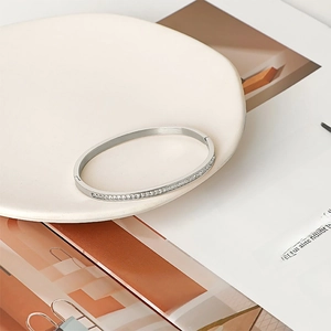 Minimalist silver-tone titanium bangle with half-circle diamond inlay on a ceramic tray