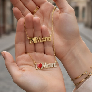 Layered gold Mama necklace and red heart pendant held by model with outdoor background