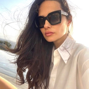 Close-up of stylish oversized black square sunglasses worn by a model in sunny outdoor setting