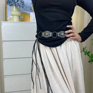 Close-up of a black Y2K vintage leather belt with metal studs and tassel details on a model