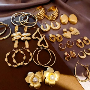 Close-up of golden geometric earrings collection including hoop and heart designs on silk