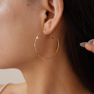 Close-up of a gold geometric hoop earring with rivet details on a side-view model