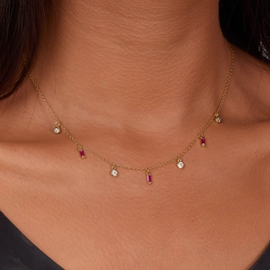 Detailed close-up of golden tassel necklace featuring red square and clear round stones
