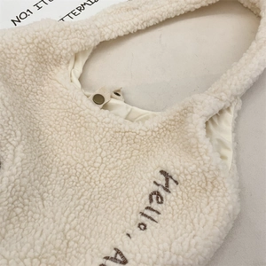 Gros plan du sac en polaire crème avec broderie 'Hello' et bouton pression vintage