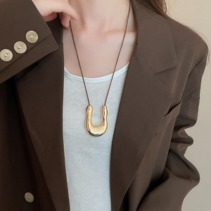 Dettaglio del ciondolo a U in oro liquido regolabile su una collana in corda marrone