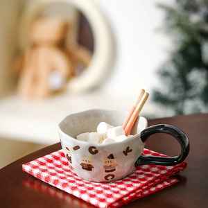 Detailed view of a ceramic bear mug with marshmallows, wavy rim, and black handle on a desk