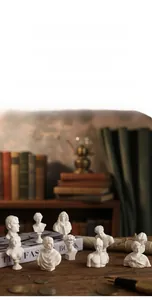 Miniature white resin bust sculptures of classical Greek figures on a wooden desk