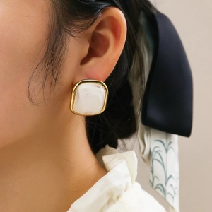 Close-up of vintage square gold earrings with white marble resin texture on model