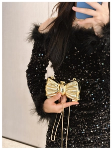 Detail of a shiny gold bow-shaped mini clutch with metal finish and chain strap