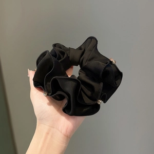 Elegant black satin scrunchie with rhinestones edge shown on hand against grey background