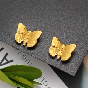 Detailed macro view of gold butterfly wing stud earrings on a dark textured surface