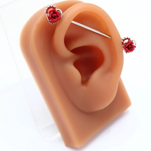Piercing industrial con rosa rossa e cuore su un modello di orecchio in silicone