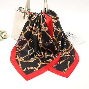 Close-up of a folded silk scarf with gold chain print draped over a luxury handbag