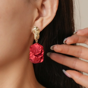 Detail of red petal tassel earrings with textured gold studs worn by a female model