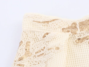 Detailed view of cream lace fabric with mesh patterns and golden sequin floral embroidery