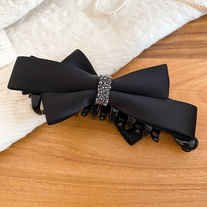 Close-up of black satin bow hair claw clip with sparkling rhinestones on wooden table