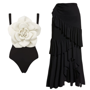 Detailed view of black swimsuit with large white 3D flower and layered ruffle skirt