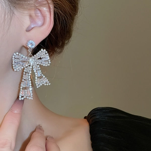 Macro view of silver bow-shaped drop earrings with brilliant cubic zirconia on model