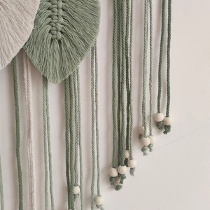Detail of bohemian woven leaf wall hanging with sage green tassels and wooden beads