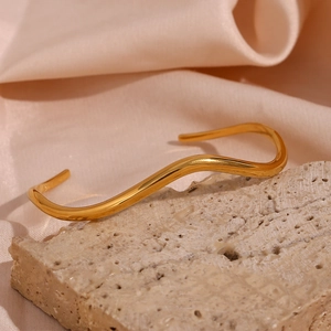 Detailed view of a gold wavy cuff bracelet resting on stone with pink silk background