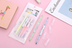 Flat lay of 6 dual-tip pastel highlighters with a notebook on a pink background