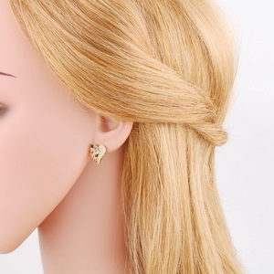 Close-up of golden heart earring with multicolored cubic zirconia on woman's ear