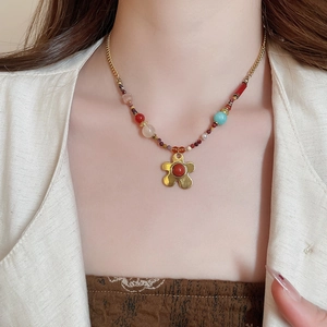 Close-up of beaded necklace with gold flower pendant on model in beige blazer
