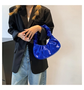 Detail of bright blue pleated cloud shoulder bag in glossy leather on model's shoulder