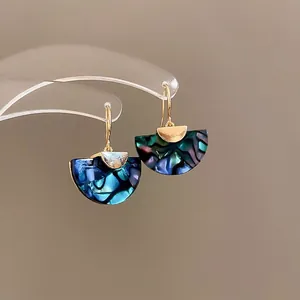 Golden fan-shaped earrings with colorful abalone shell inlays on a clear acrylic stand